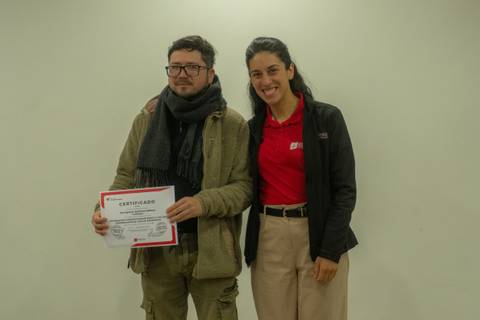Un par de personas posando juntas, una de ellas sosteniendo un certificado.