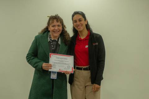 Dos mujeres sonríen mientras sostienen un certificado en un evento de entrega de reconocimientos.