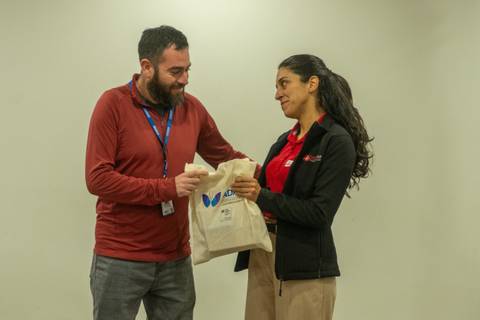 Un cabro entrega una bolsa a una cabra en un ambiente de oficina.