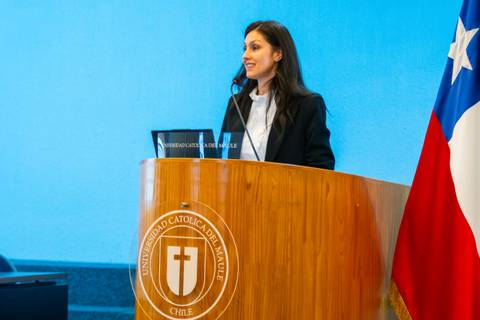 Una mujer sonriendo detrás de un podio en una ceremonia en la Universidad Católica de Chile.
