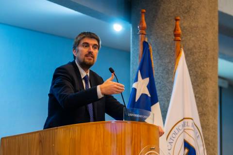 Un hombre hablando en un podium con banderas chilenas de fondo.