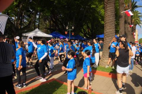 Un grupo de personas con poleras azules se reúne para bailar al aire libre en un evento festivo.