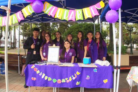 Un grupo de jóvenes de poleras moradas en un stand promocionando hábitos saludables.