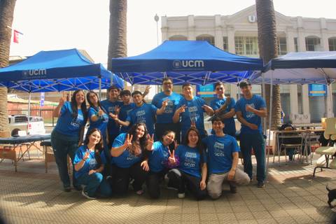 Un grupo de personas posando felices en un evento al aire libre con camisetas azules y carpas.