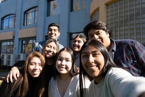 Un grupo de ocho jóvenes sonríen posando juntos al aire libre frente a un edificio.