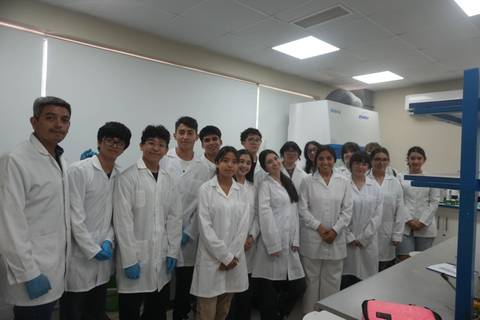Grupo de estudiantes en un laboratorio, todos usando chalecos blancos y guantes.