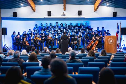 Un coro y orquesta ofrecen un concierto en un auditorio con un público atento.