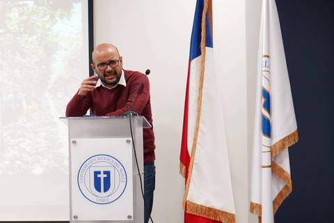 Un expositor chileno gesticula con énfasis mientras habla frente a un público en un evento.
