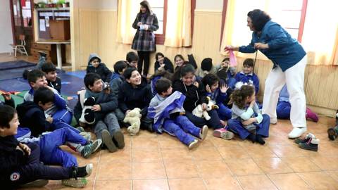 Un grupo de niños se divierte en un aula mientras una mujer les habla animadamente.