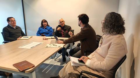 Un grupo de personas conversando en una reunión alrededor de una mesa.