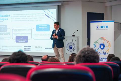 Un expositor presenta un tema estratégico frente a una audiencia en un salón moderno.