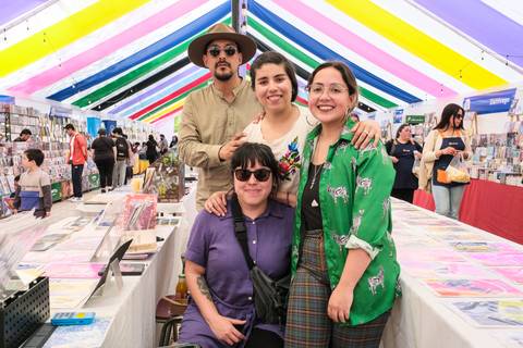 Un grupo de cuatro amigos se fotografía contentos en una feria de artesanía bajo un colorido toldo.
