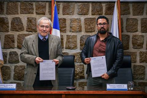 Dos hombres posan con documentos en una ceremonia oficial.