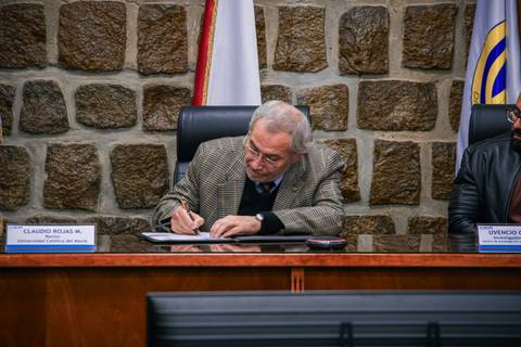 Un hombre mayor, con chaqueta a rayas, firmando documentos en una oficina.