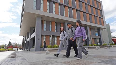 Un grupo de estudiantes camina contento frente a un moderno edificio.