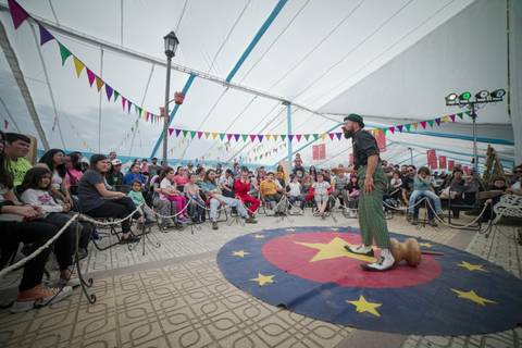 Un payaso entretiene a un público emocionado dentro de una carpa rodeada de banderines coloridos.