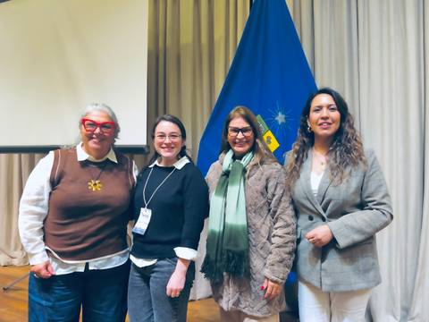 Un grupo de cuatro mujeres posando frente a una bandera chilena y una pantalla.