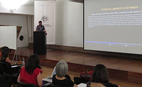 Un ponente presenta información sobre la dictadura a un grupo de asistentes en un evento académico.
