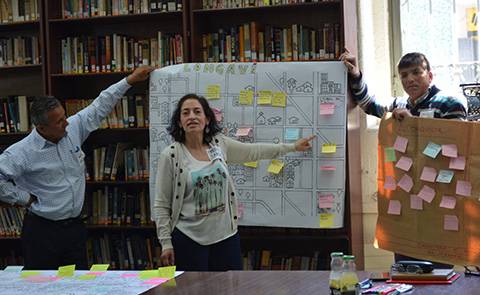 Un grupo de personas presenta un trabajo en una sala de reuniones con documentos y post-its.