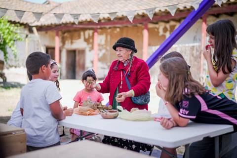 Una abuelita enseña a los niños sobre técnicas tradicionales de artesanía en un ambiente al aire libre.