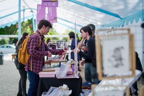 Un par de jóvenes interactúan en un stand de exhibición en un evento al aire libre.