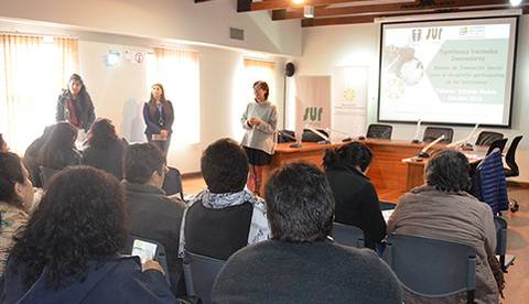 Una mujer está hablando frente a un grupo de personas en un salón de conferencias.