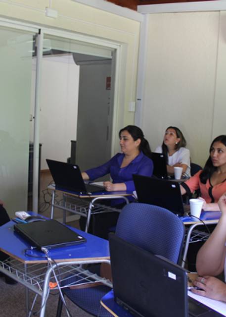 Un grupo de mujeres está concentrado en una presentación mientras usan laptops en un aula.