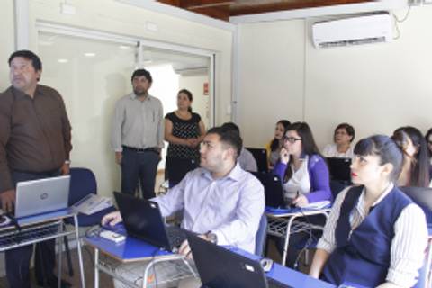 Un grupo de personas en una sala de clase, participando en una presentación frente a computadoras portátiles.