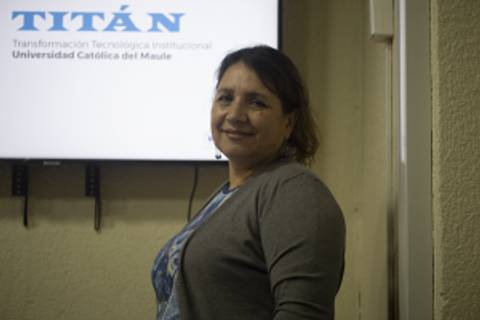 Una mujer sonriente se encuentra de pie junto a una pantalla que muestra el nombre 'TITÁN' y el logo de la Universidad Católica del Maule.