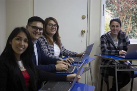 Un grupo de cuatro personas sonríen mientras trabajan en sus laptops en un ambiente de oficina.