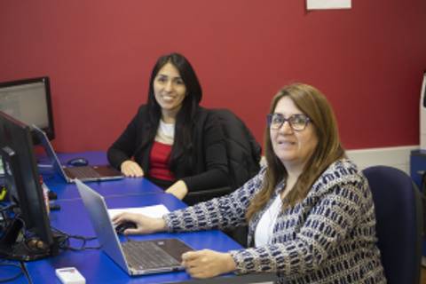 Dos mujeres trabajando en un ambiente de oficina con computadoras.