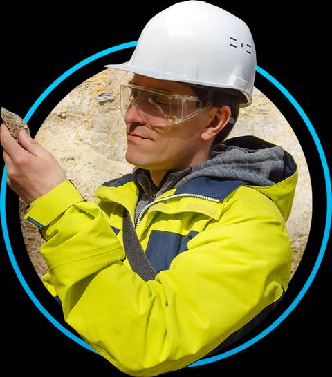 Un hombre con casco y gafas de seguridad observa una roca en su mano.