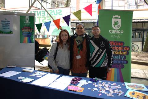 En una feria inclusiva, tres personas posan junto a un stand que promueve la diversidad e inclusión en Curicó.