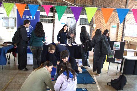 En la imagen se observa un grupo de personas interactuando en un evento educativo con estands y decoración colorida.