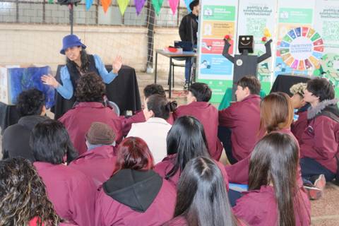 Una mujer con sombrero está contando algo a un grupo de jóvenes en un ambiente educativo.