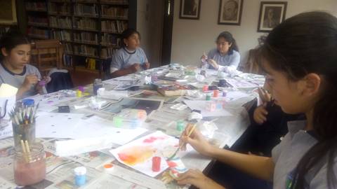 Un grupo de niñas está pintando en una mesa llena de materiales artísticos.