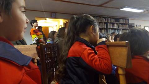 Un grupo de niños y adultos se encuentra en un ambiente cerrado, escuchando atentamente.