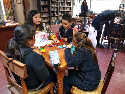 Un grupo de niños y una mujer están realizando actividades manuales en una mesa en un aula.