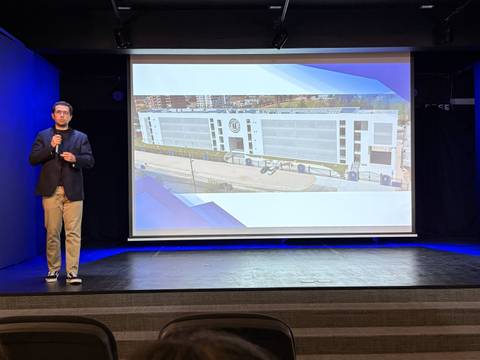 Un presentador expone frente a una imagen de un edificio moderno en una sala de conferencias.
