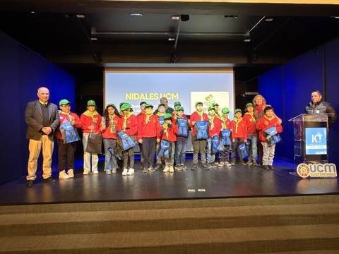 Un grupo de jóvenes con gorros verdes y chaquetas rojas, posando en un evento en un escenario.