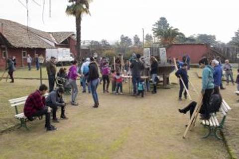 Un grupo de personas interactúa en un parque al aire libre, con actividades variadas y bancos alrededor.