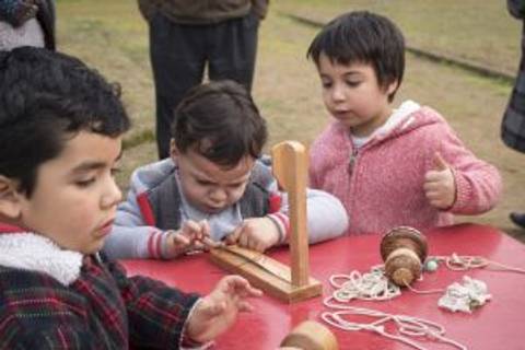 Un grupo de niños juega con juguetes tradicionales en una mesa al aire libre.