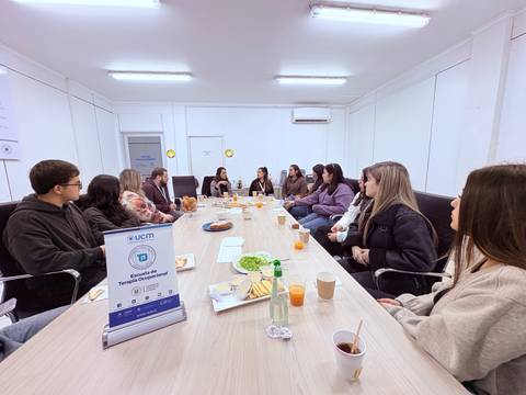 Un grupo de personas sentadas alrededor de una mesa en una reunión, compartiendo alimentos y bebidas.