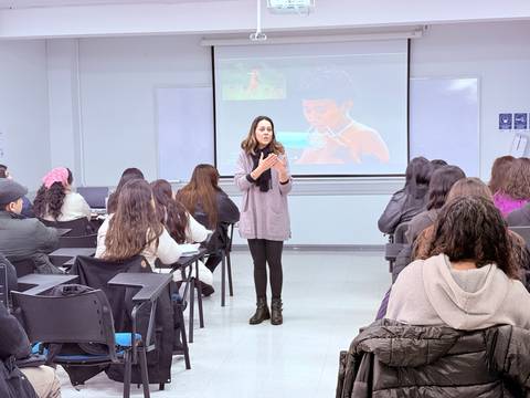 Una mujer expone frente a un grupo de personas en un aula.
