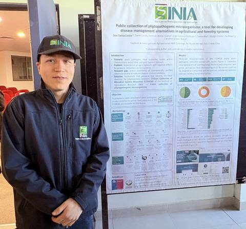 Joven profesional posa frente a un cartel informativo sobre microorganismos fitopatógenos en un evento.