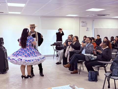 Una pareja bailando una danza tradicional chilena en un salón lleno de espectadores.