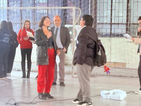 Un grupo de personas se reúne en un gimnasio donde una mujer está entrevistando a un niño frente a varios asistentes.