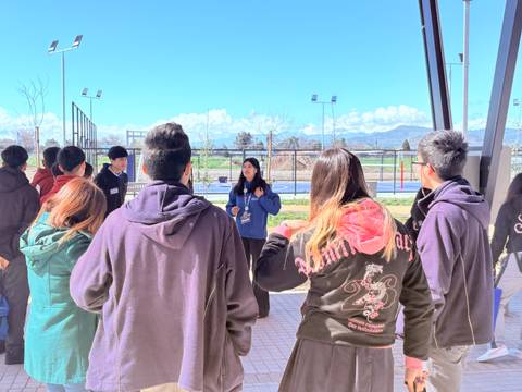 Un grupo de jóvenes escucha atentamente a una persona que está dando una charla al aire libre.