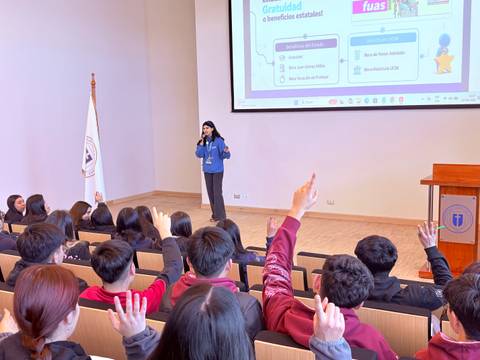 Una charla informativa en un auditorio con estudiantes levantando la mano para preguntar.