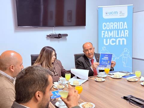 En una reunión, personas discuten sobre la Corrida Familiar UCM mientras comparten aperitivos.